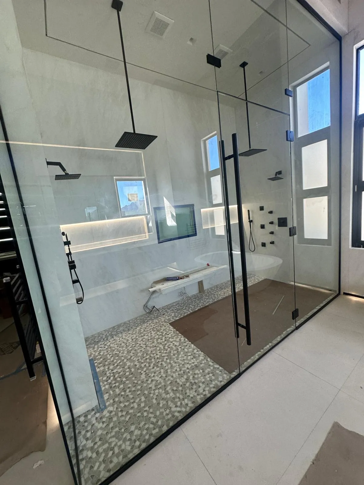 Frameless glass shower with black frame and pebble stone floor in a Phoenix AZ bathroom remodel by RDC Renovation