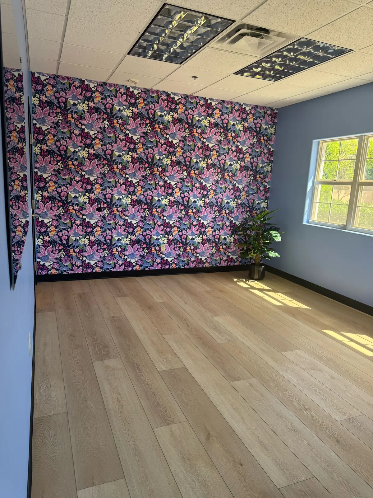 Wood-look LVP flooring that RDC Renovation installed in a Phoenix, AZ clinic room, shown with a floral wallpaper wall