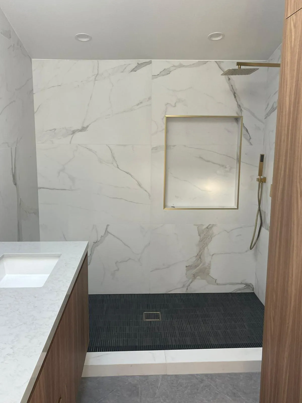 Marble look large format tile shower with gold fixtures and a built-in bench by RDC Renovation in Phoenix AZ
