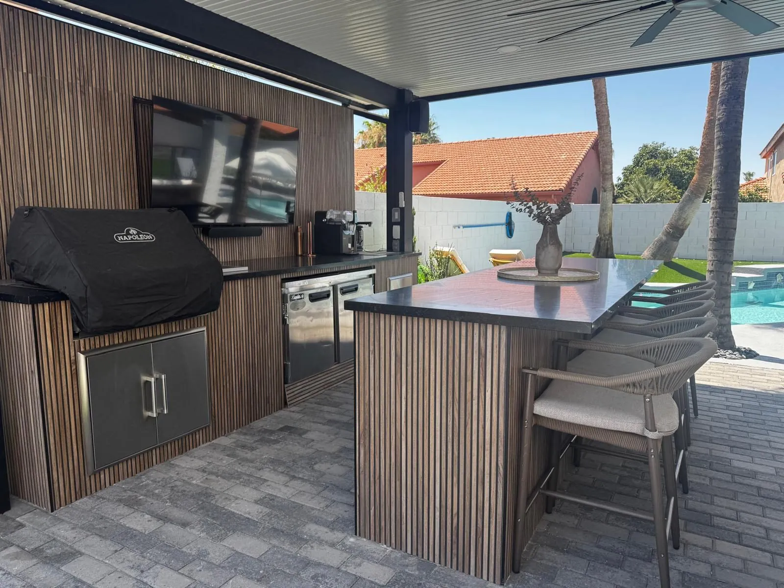 Custom outdoor kitchen with built-in BBQ grill slat wood bar black granite countertop and TV by the pool Phoenix AZ